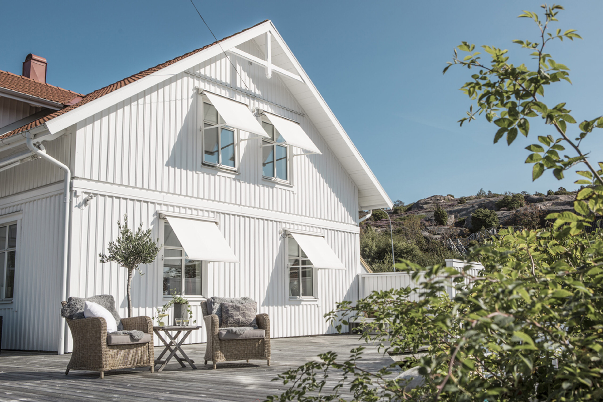 Mørkt hus med stripete vindusmarkiser og terrassemarkise